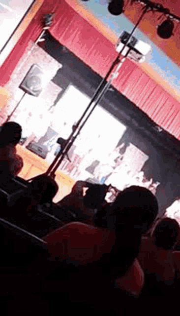 a group of people sitting in front of a stage with a red curtain .