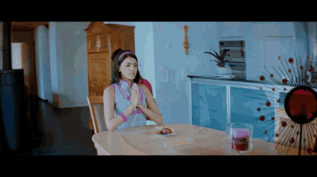 a woman sits at a table with her hands together