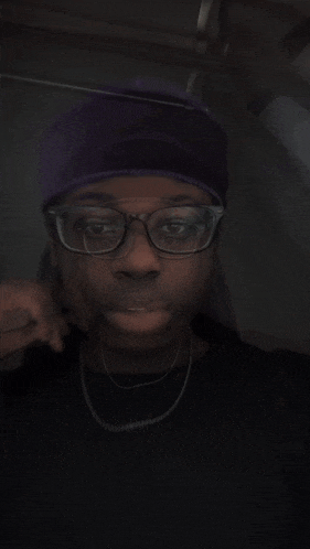 a young man wearing glasses and a purple headband looks at the camera