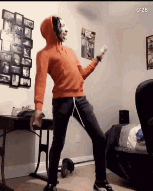 a man wearing headphones and an orange hoodie is dancing in a room