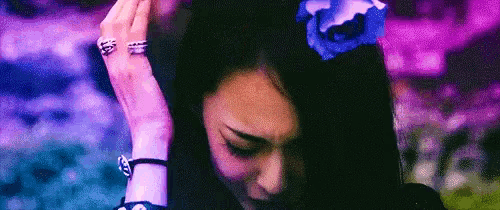 a woman with a blue flower in her hair is covering her face with her hand .