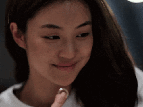 a close up of a woman 's face with a white pearl on her finger