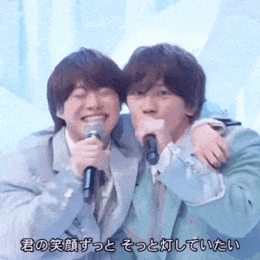 two young men are hugging each other while holding microphones .