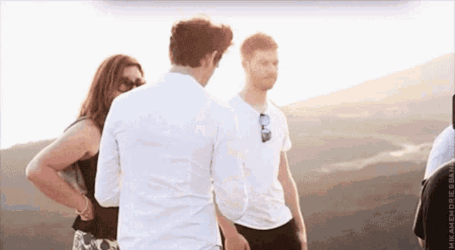 a man in a white shirt stands in front of a woman and a man in sunglasses