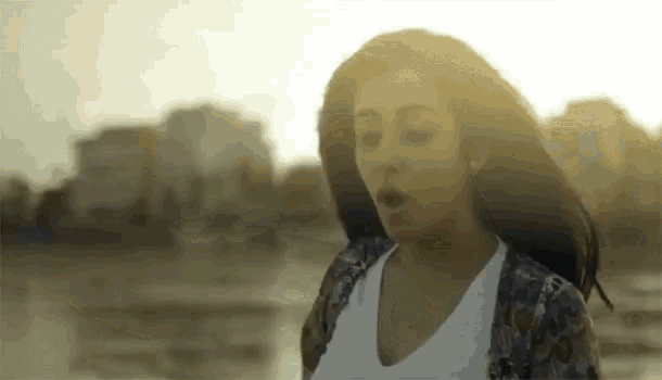 a woman is standing in front of a body of water with her hair blowing in the wind .