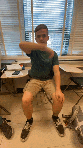 a boy is sitting in a chair with his arm outstretched in front of a window