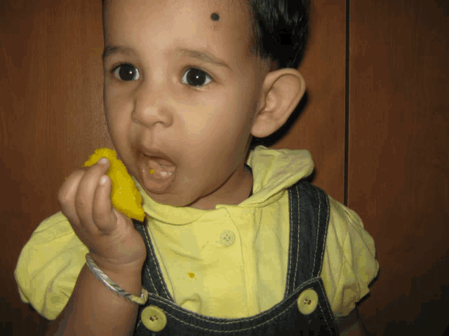 a young boy with a black spot on his forehead eating a piece of food