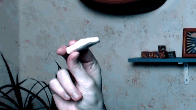 a person is holding a piece of chalk in their hand in front of a shelf
