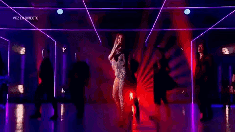 a group of people are dancing on a stage with purple lights behind them .