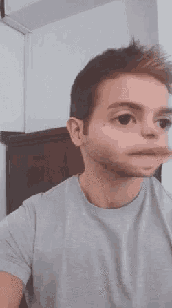 a man in a gray shirt is making a funny face with his mouth open .