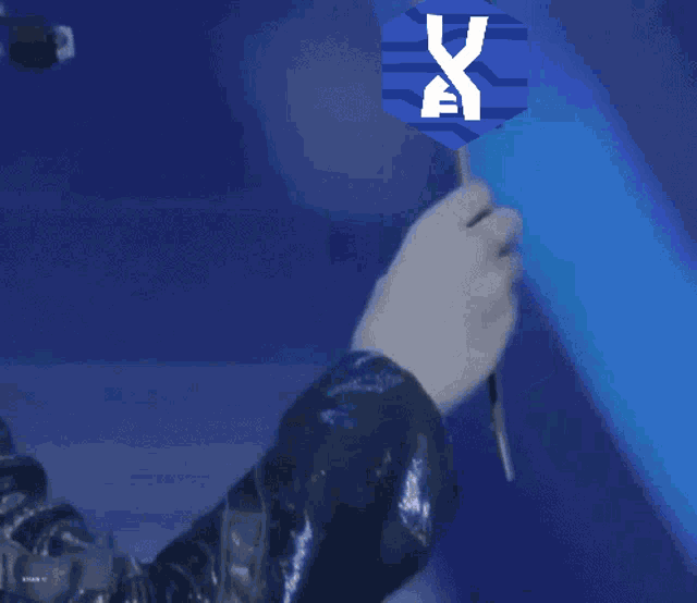 a person wearing a microphone is holding a blue sign that says x