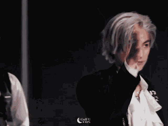 a man with white hair is covering his face with his hand while wearing a black suit
