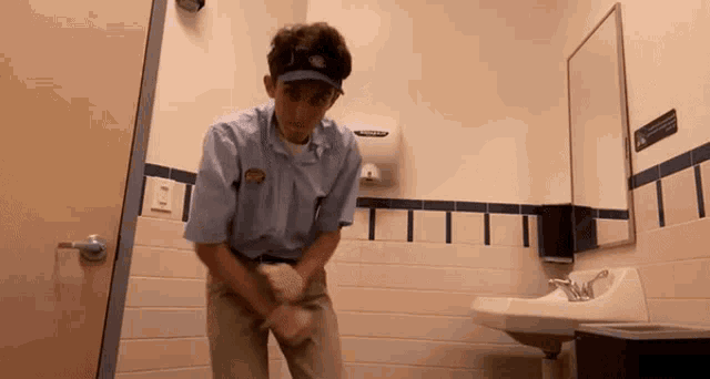 a man in a blue shirt and visor is cleaning a bathroom sink