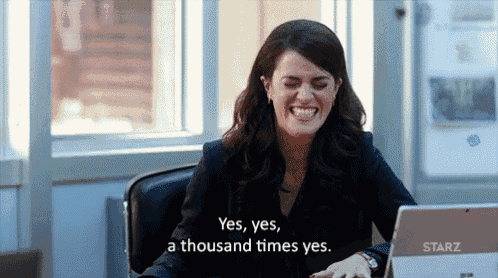 a woman is sitting at a desk with a laptop and laughing while saying yes yes a thousand times yes .