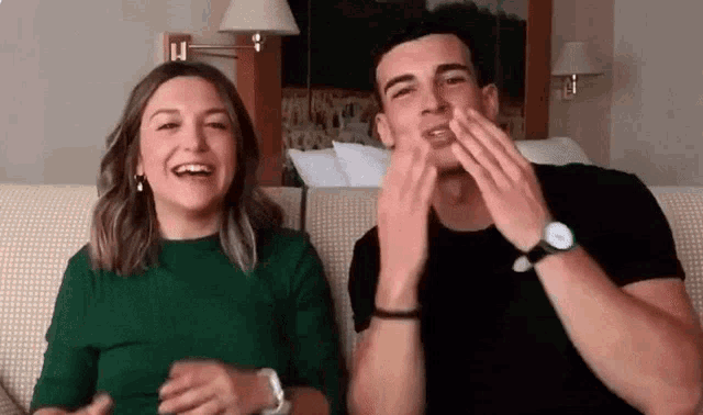 a man and a woman are sitting on a couch with their hands on their faces .