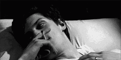a man is laying in bed smoking a cigarette and holding his nose .