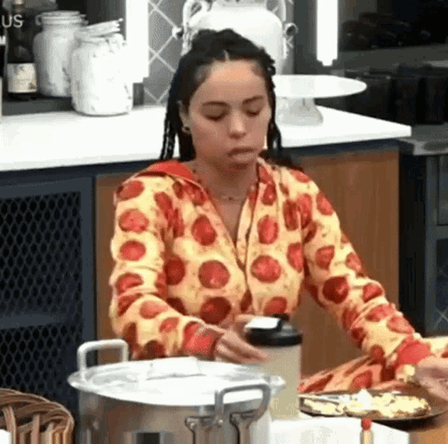 a woman in a pizza shirt is sitting at a table with a pot of food and a plate of food .