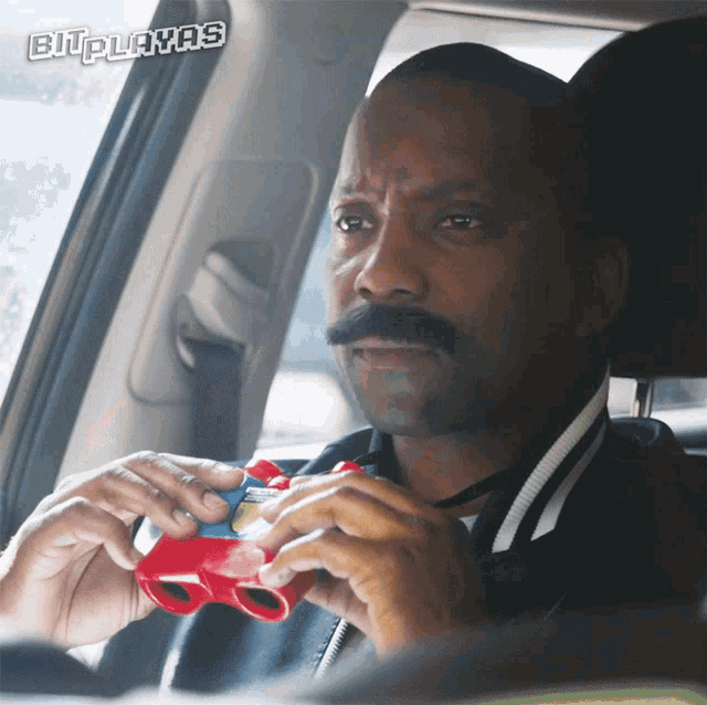 a man with a mustache is sitting in a car playing a video game with the words bitplayas above him