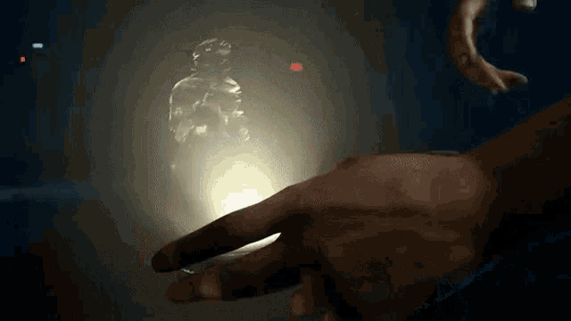 a person 's hand is reaching out towards a glowing object in the dark .