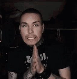 a man with a tattoo on his arm is holding his hands together in front of a microphone and smiling .