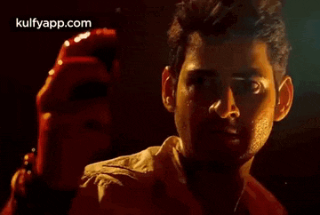 a close up of a man 's face in a dark room with a hand behind him .
