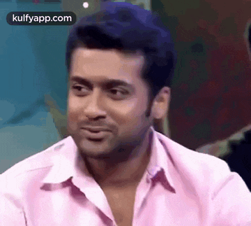 a man in a pink shirt is making a funny face while sitting down .
