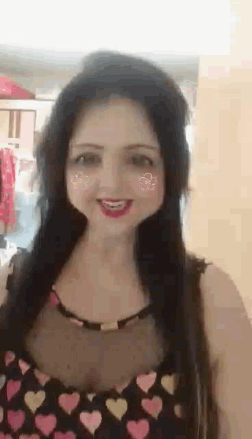a woman wearing a heart print top is smiling and making a face .