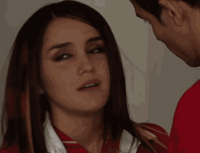 a close up of a woman 's face with a man in a red shirt