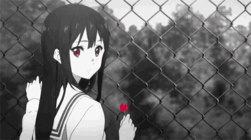 a girl in a school uniform is holding a red lollipop and looking over a chain link fence .