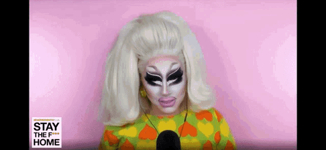 a drag queen is talking into a microphone while wearing a yellow and orange shirt with hearts .