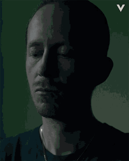 a man 's face is shown in a dark room with the letter v in the corner
