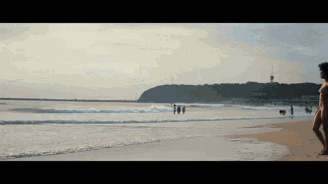 a woman in a bikini stands on a beach near the ocean