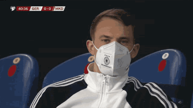 a man wearing a face mask is watching a soccer game between ger and mkd