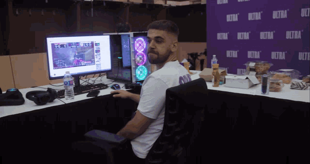 a man sitting in front of a computer with a purple wall that says ultra on it