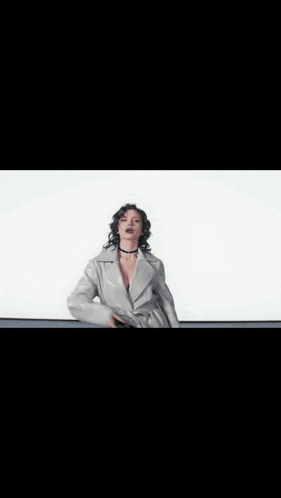 a woman in a white coat is standing in front of a white wall .