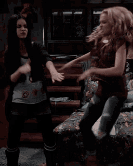 two girls are dancing in a bedroom with a book on the bed between them