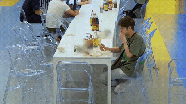 a man sits at a long table with a bottle of orange juice