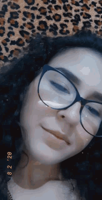 a girl wearing glasses is laying on a leopard print blanket .