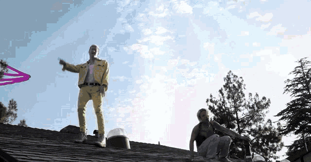 a man in a yellow jacket is standing on a roof while a woman sits on the ground