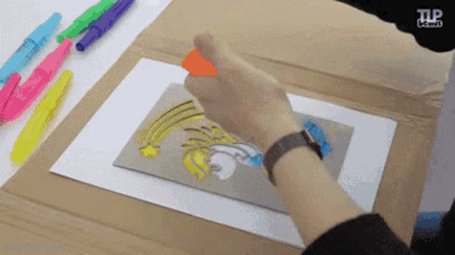 a person is drawing a picture on a piece of cardboard with a tlp logo in the corner