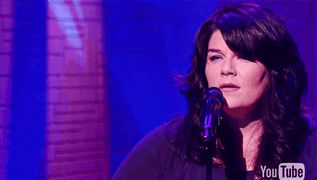a woman singing into a microphone with the youtube logo in the background