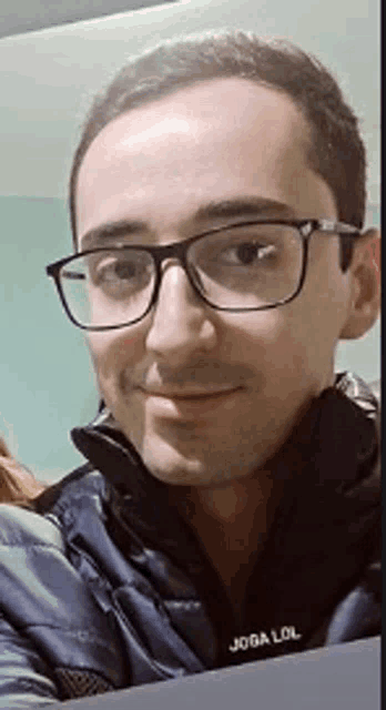 a young man wearing glasses and a blue jacket is smiling for the camera .