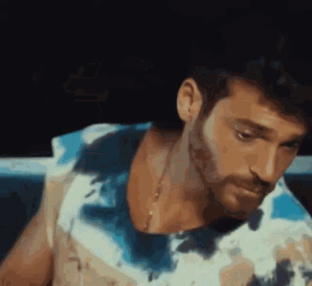 a man with a beard is wearing a blue and white tie dye shirt and looking down .