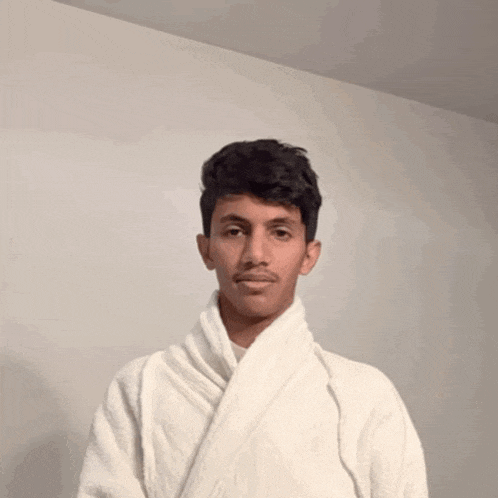a young man is wearing a white robe and looking at the camera