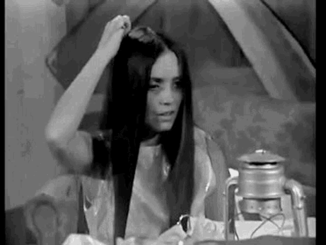 a black and white photo of a woman brushing her hair in front of a lantern .