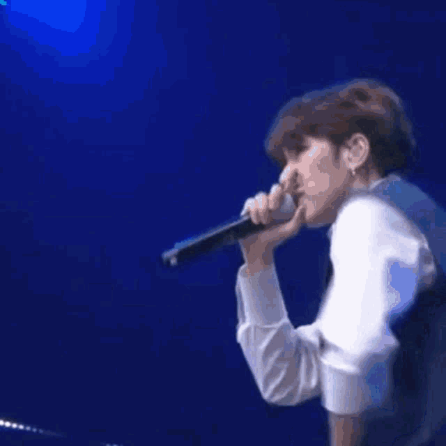 a man in a blue jacket is singing into a microphone while two other men are dancing .