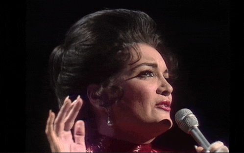 a woman singing into a microphone with her hands in the air