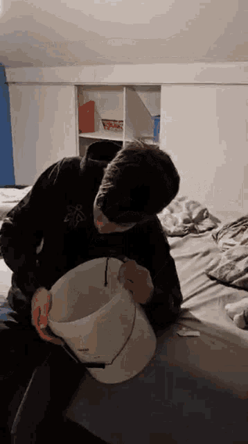 a man is sitting on a bed holding a white bucket with the word bucket on it