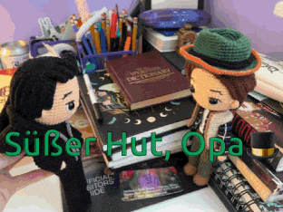two stuffed dolls are sitting on a desk with a stack of books and a dictionary