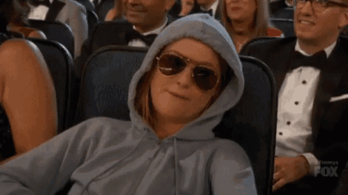 a woman wearing sunglasses and a hoodie is sitting in a crowded theater .